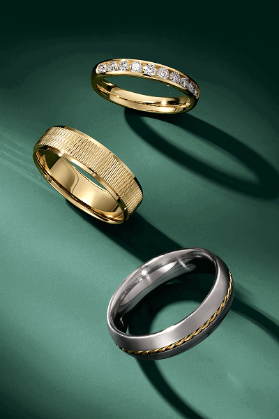 Three men’s wedding bands on green background.