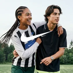 Twee jonge mensen lopen op een voetbalveld, de een met zijn arm om de ander, beiden dragen sportkleding en lachen.