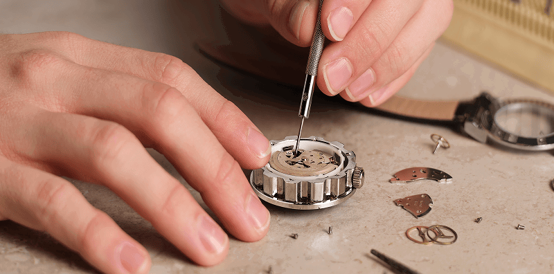 Close-up of jeweler repairing a watch on workbench.