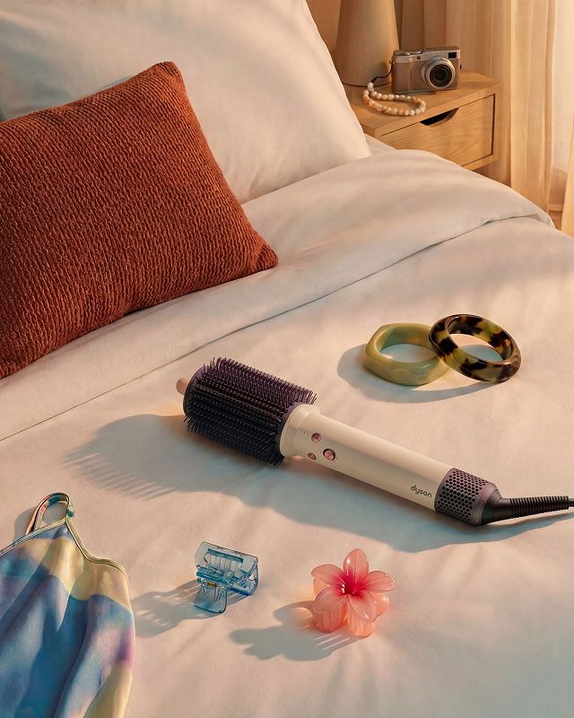 Dyson Airsmooth styling brush on a hotel bed.