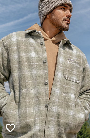 A man wearing a tan sweatshirt and shacket against a blue sky.