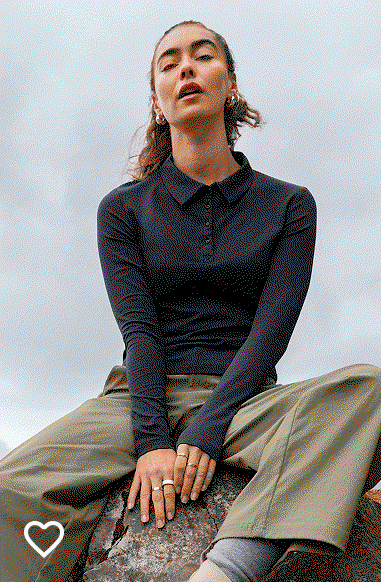 A woman sitting on a rock, wearing a black shirt and green pants.