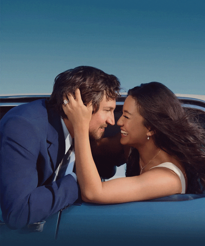 Smiling newlywed couple embracing in a car, with the bride’s diamond wedding rings visible.