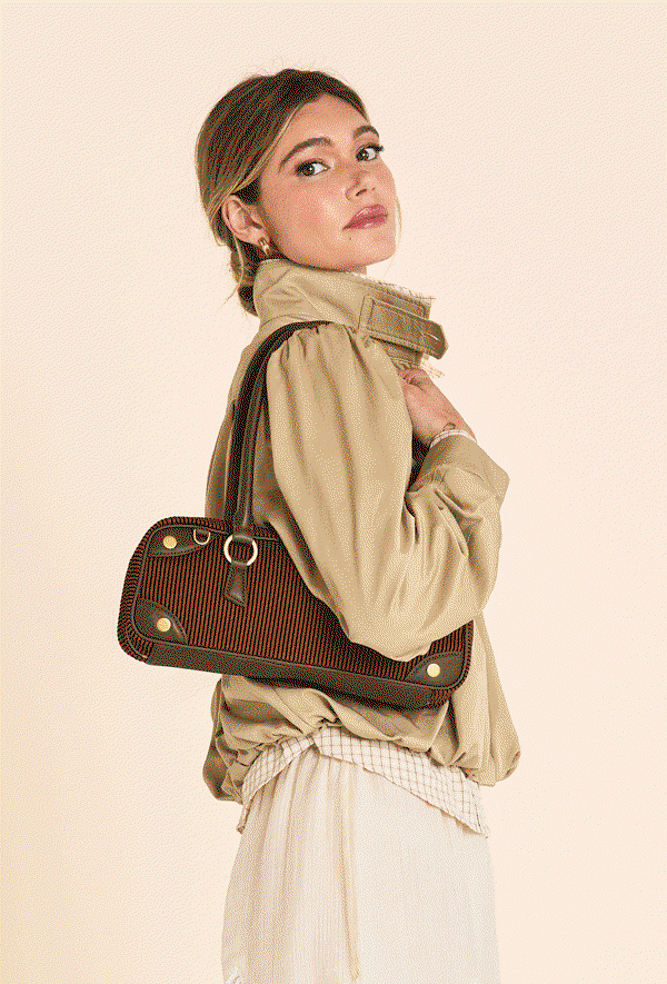 Alt text: Model carrying the Meredith Sml in Tuscan Tandem, featuring terracotta and espresso stripes with rich green leather trim and gold hardware.