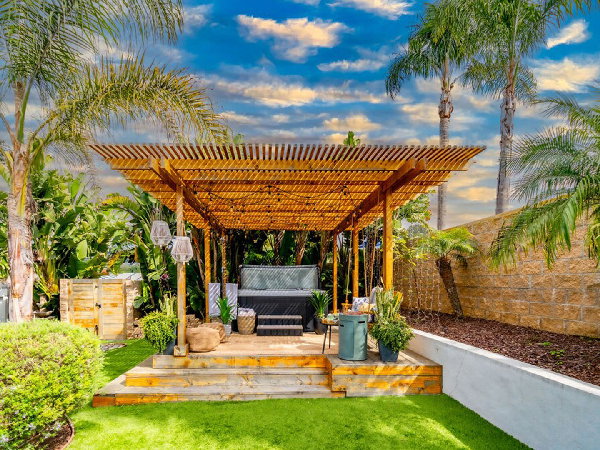 Cozy outdoor pergola retreat with hot tub, lush palms, and landscaped garden.