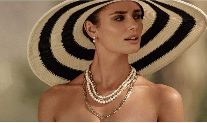 Model Paulina Taylor wear wide brim hat and layered pearl and gold chain necklaces.