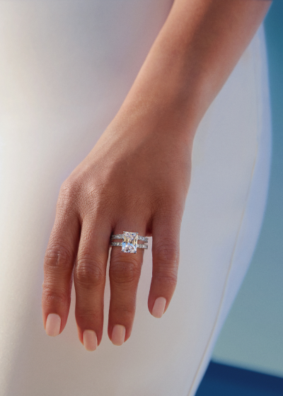 Close-up of a woman’s hand wearing a radiant-cut diamond engagement ring and diamond wedding band.