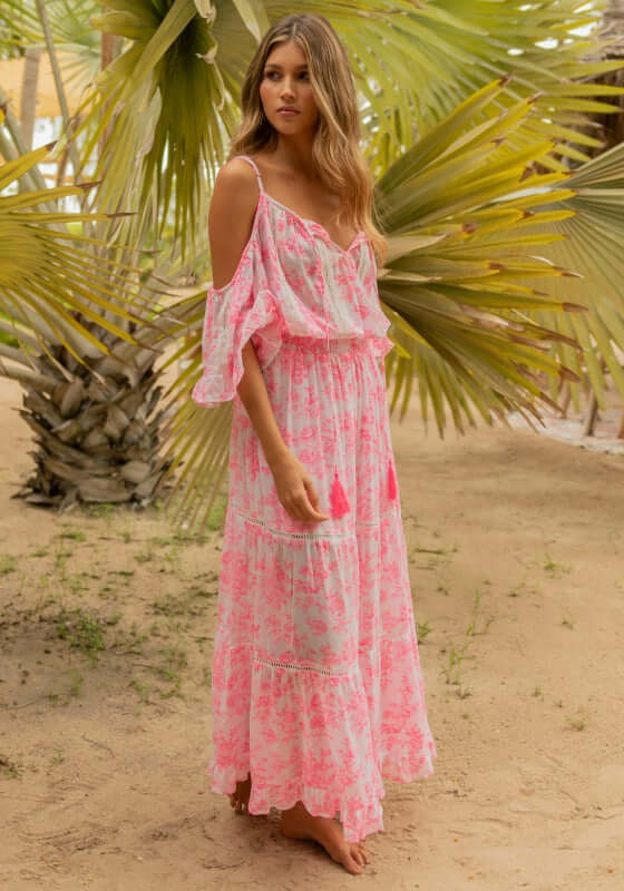 Woman in a pink embroidered dress with a tie waist stands against a rocky backdrop.