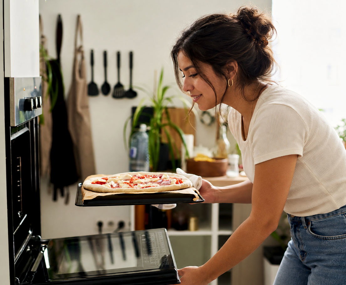 Woman places a freshly prepared pizza into an open oven in a bright kitchen
