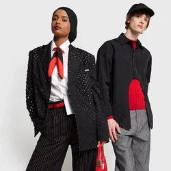 Twee modellen staan zij aan zij. Het vrouwelijke model draagt een gestructureerde zwarte blazer, gestreepte broek en rode accenten. Het mannelijke model draagt een zwart shirt, een rode trui en een grijze broek.