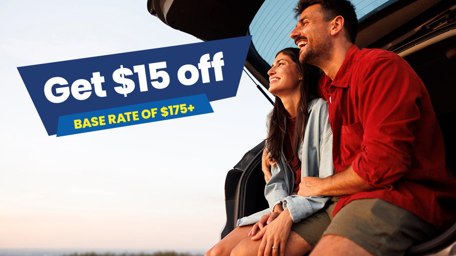 Get $15 off base rate of 175+. Two people sitting at the open rear of an SUV during sunset. 
