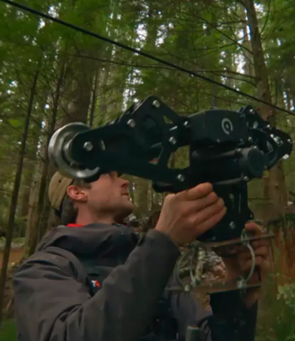 Videographer mounting a GoPro cable cam rig to a line in the forest.