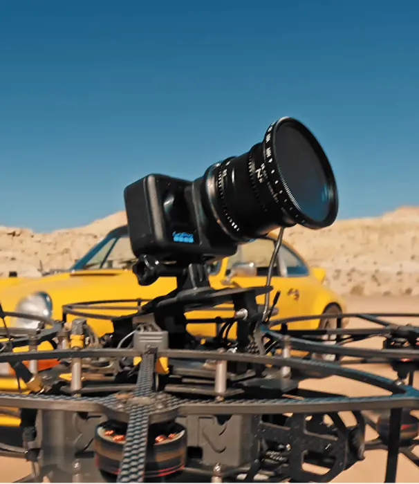FPV drone mounted with a GoPro camera in a desert setting with a yellow car in the background.