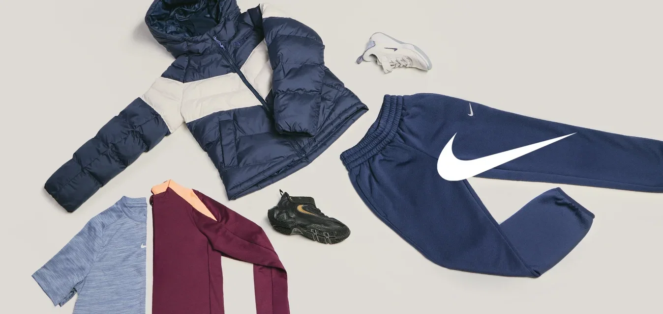Donkerblauwe en beige gewatteerde jas, blauwe en kastanjebruine overhemden, marineblauwe joggingbroek, zwart-witte sneakers gerangschikt op een lichte achtergrond.