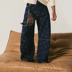 Jonge man die op een lage tan leren bank staat, gekleed in een crème cardigan en wijde marineblauwe broek, terwijl hij zijn hoed aanraakt in een minimalistische witte kamer.