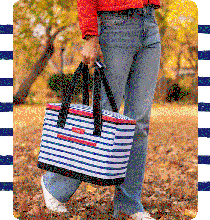 Person carrying a black and white striped SCOUT tote bag filled with snacks and a white scarf in an autumn park.