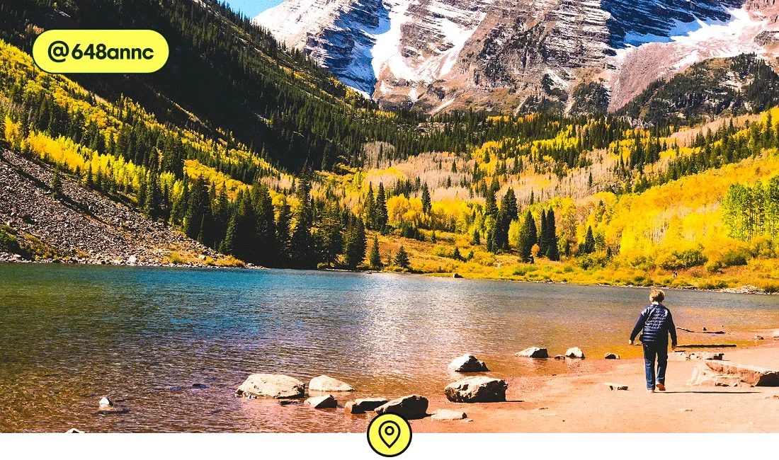 Image description: A person on the edge of a lake with fall foliage on a mountainside in the background, photo taken by @648annc