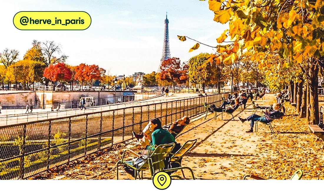 Image description: People sitting along the Seine in fall with the Eiffel Tower in the background, photo taken by @herve_in_paris