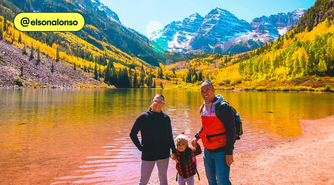 Image description: Two adults and a child standing in front of a lake with yellow aspens in the background, photo taken by @elsonalonso