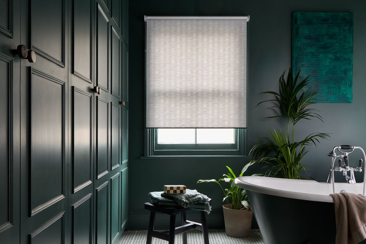 Light-filtering Roller blind at a recessed bathroom window, complementing dark panelled walls, indoor plants and a freestanding bath.