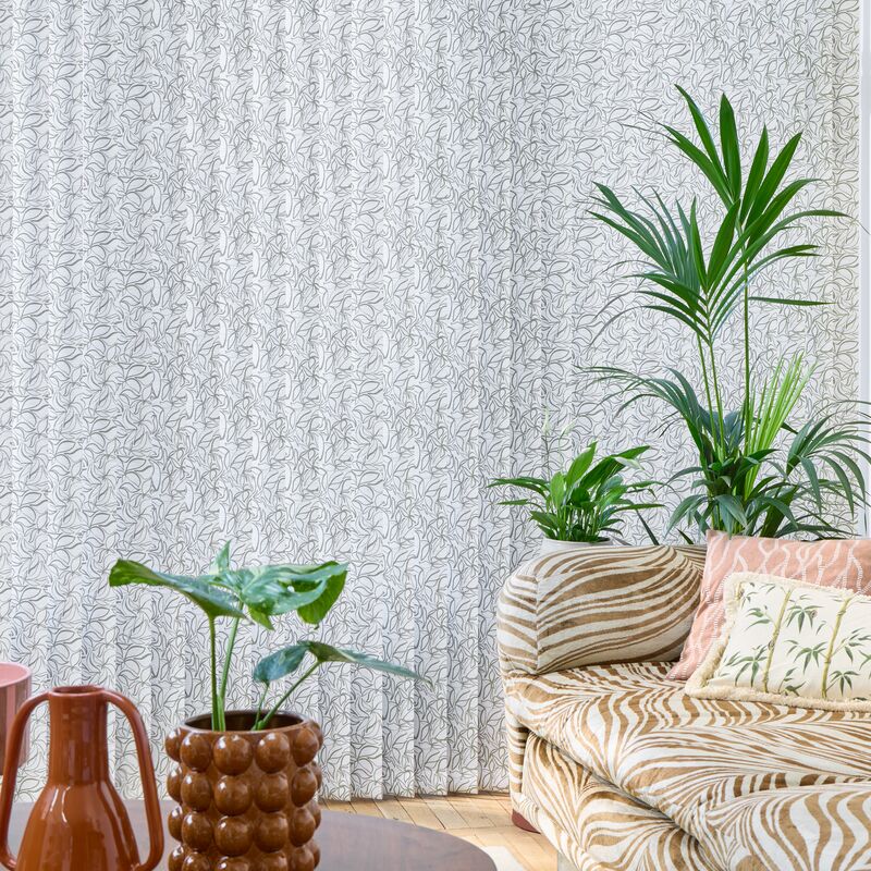 Floor-to-ceiling vertical blinds with a delicate leaf pattern create a soft backdrop in a bright living space with plants and a striped sofa.