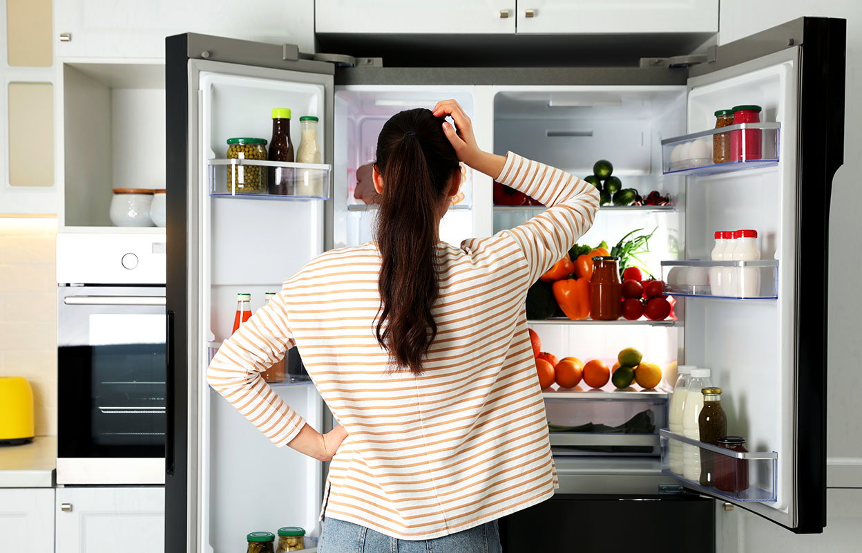 A homeowner scratching their head in front of an open fridge