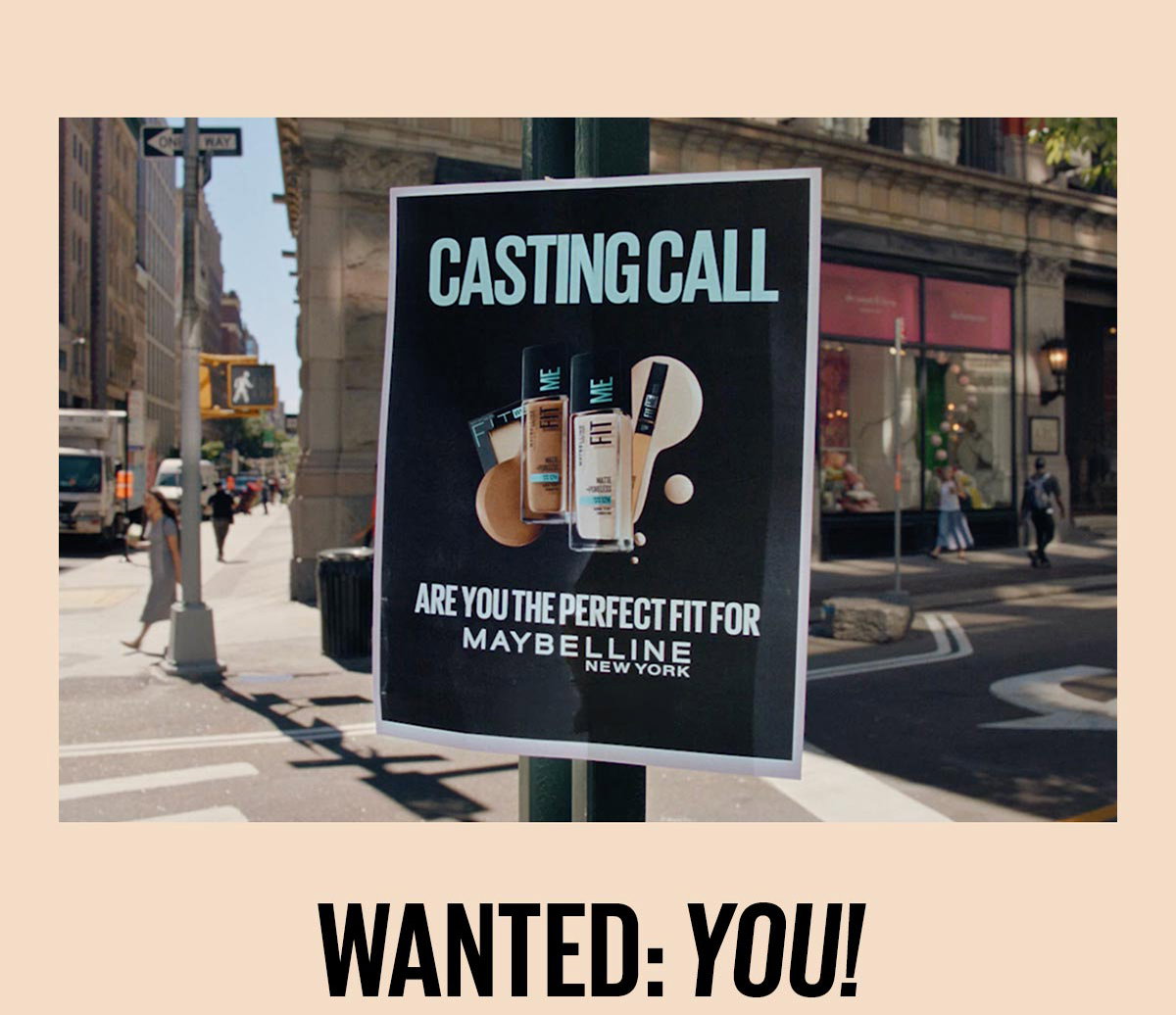 A black Maybelline Fit Me casting-call poster with Fit Me Matte + Poreless Foundation bottles on it posted on a city street pole promotes an in-person shade-matching event happening in New York City on September 13th, inviting consumers to find their perfect foundation fit. Below the image is a headline that reads Wanted: You!.