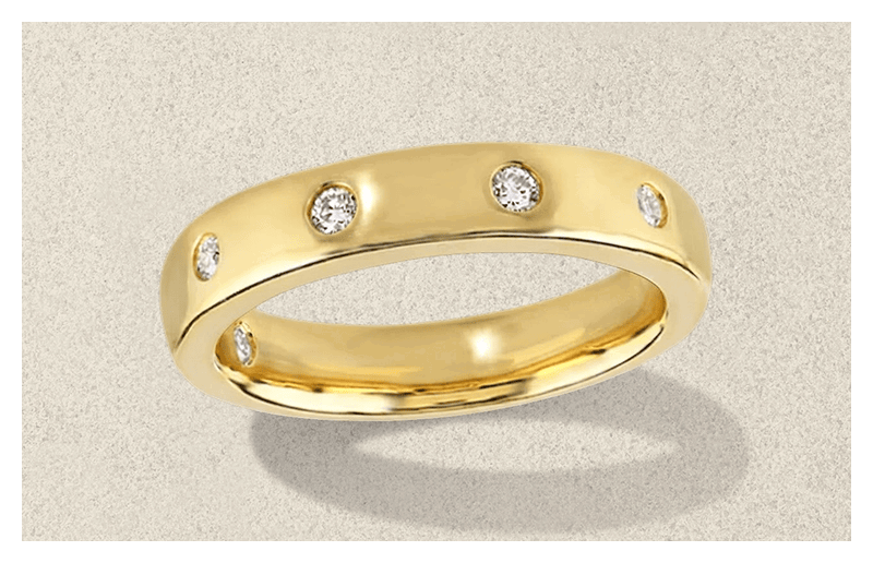 Gold wedding band with diamond accents on textured background.
