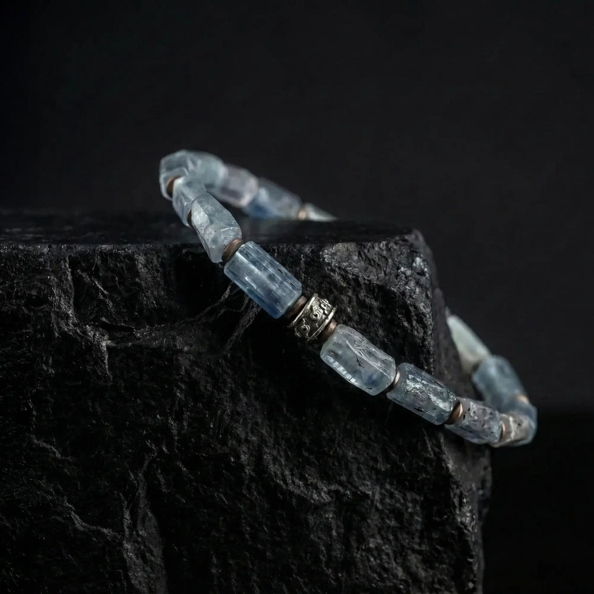 Kyanite Bracelet VII, with slender 6mm blue stones, draped over dark rock.