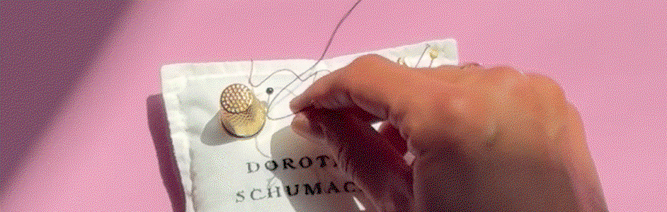 Eine Nahaufnahme eines dunkelblauen Textil-Labels von DOROTHEE SCHUMACHER auf zartem rosa Hintergrund. Das Label zeigt einen elegant geschwungenen, gestickten 'Love'-Schriftzug, verfeinert mit einem Edelweiß-Motiv und dem Schriftzug 'SINCE 1989'.