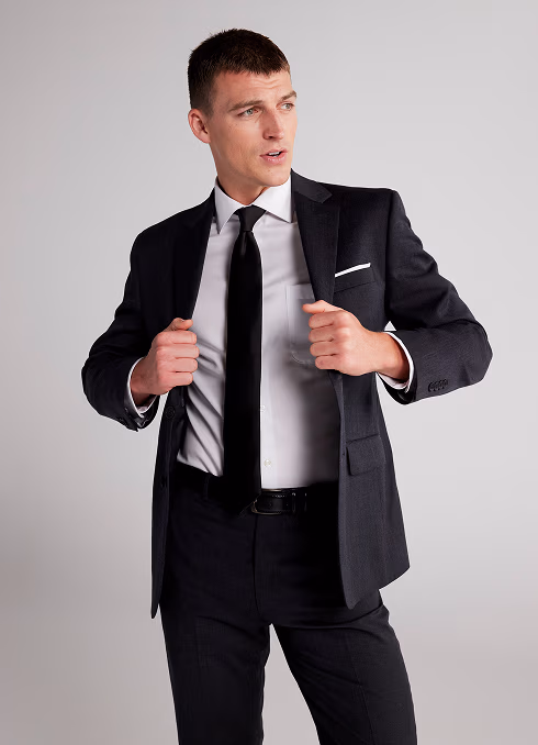 A young man posing in a modern black suit with a black tie.