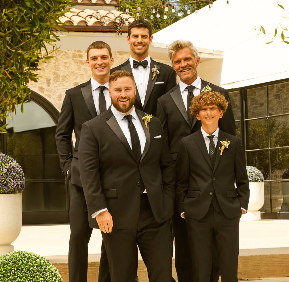 A group of five men of varying ages dressed in black suits and tuxedos for a wedding.