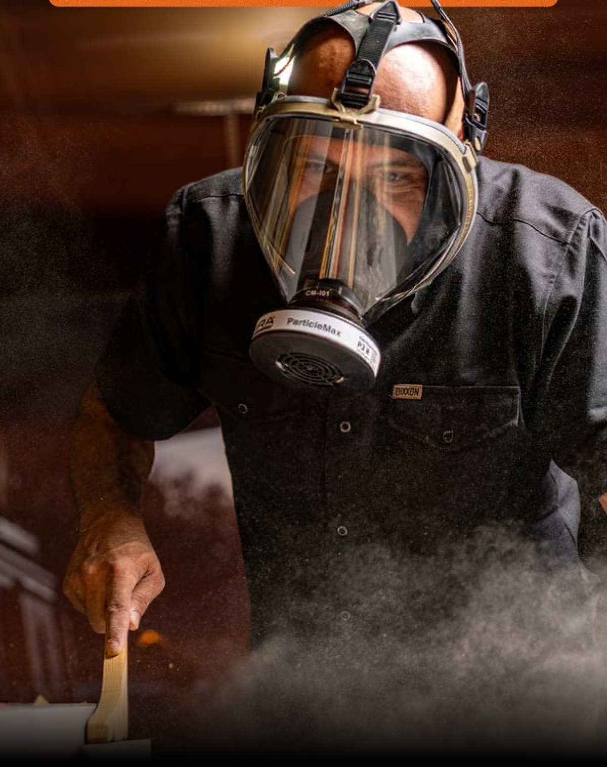 A person wearing a full-face respirator mask is stirring a mixture in a bowl.