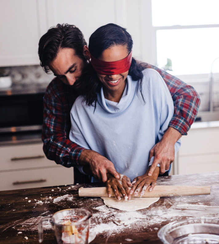 A smiling couple make a pie with one person blindfolded.