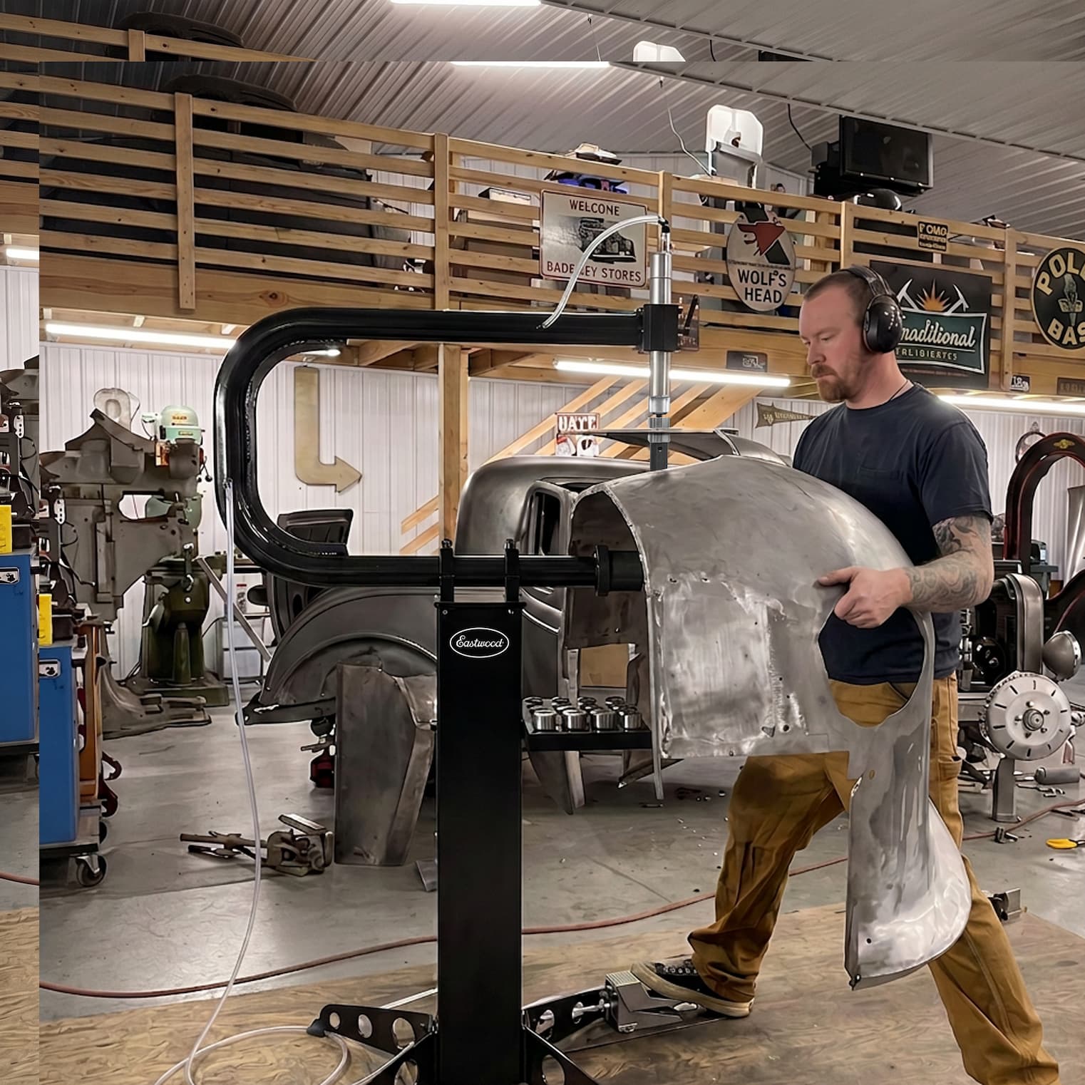 Person shaping a vehicle body panel with a fabrication machine in an auto workshop.