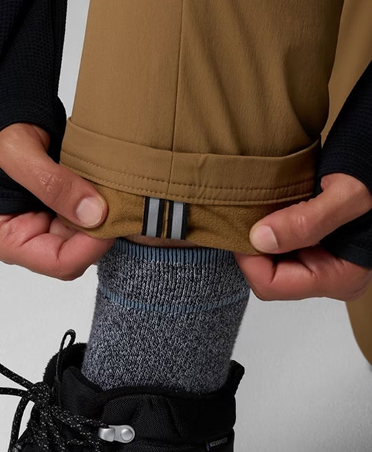 A model flipping up the cuff of their brown pant leg to reveal the reflective details.