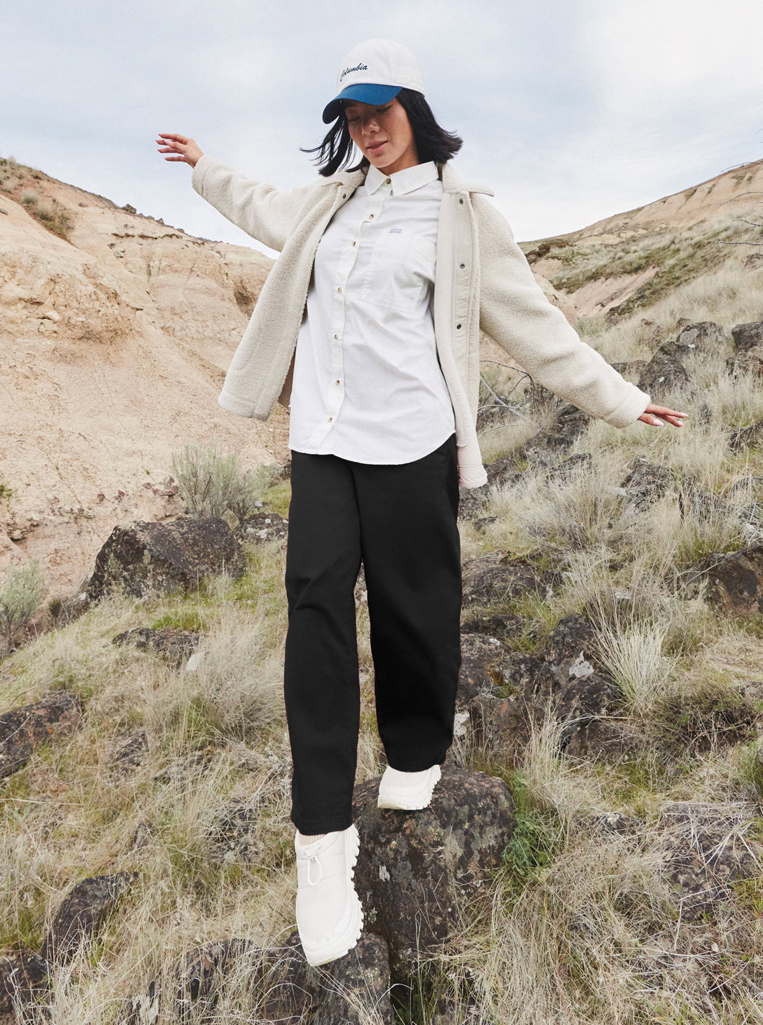 A woman standing outside wearing black pants, a white shirt, and jacket.