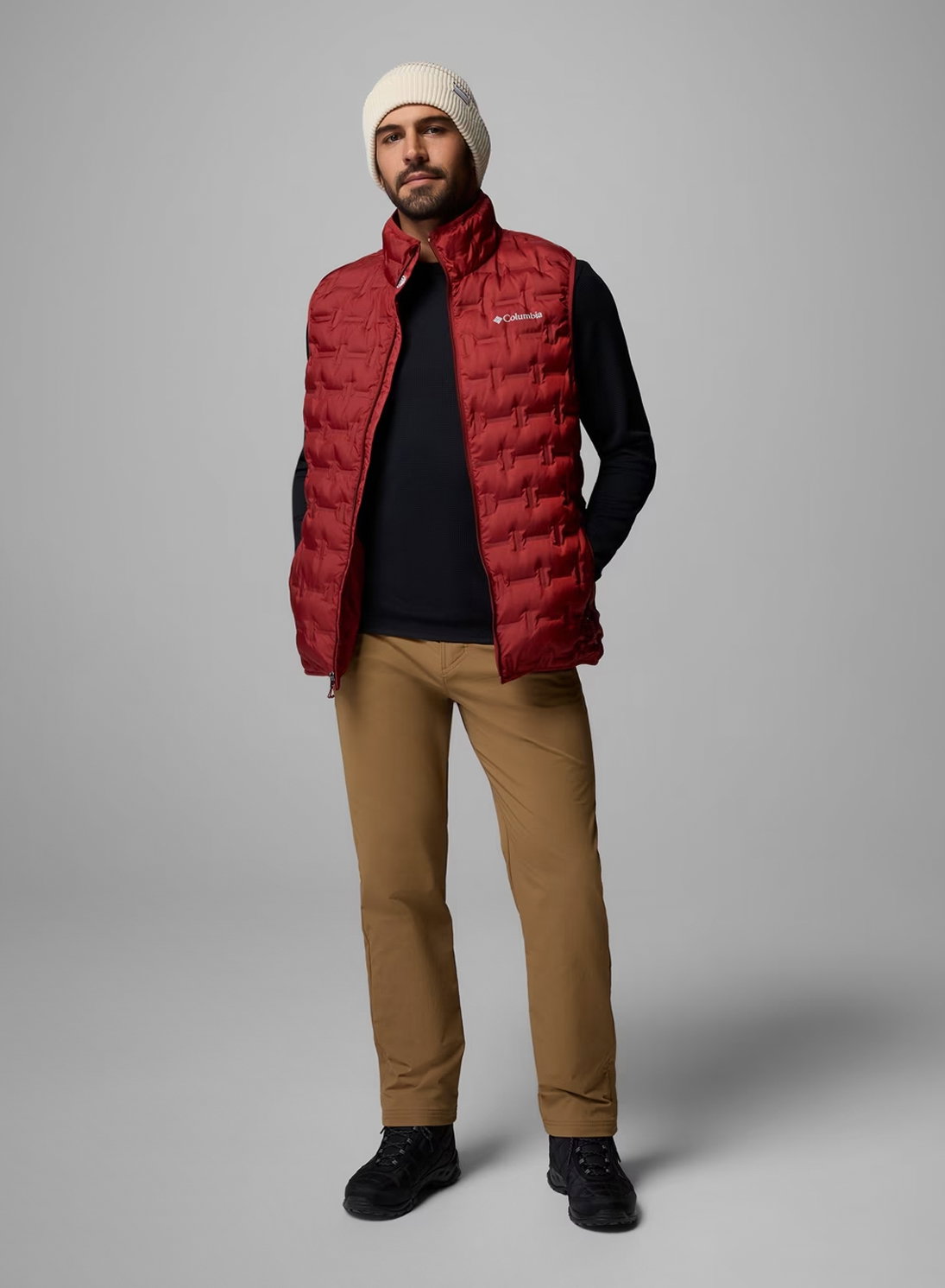 A man wearing a black shirt, red vest, and brown pants.