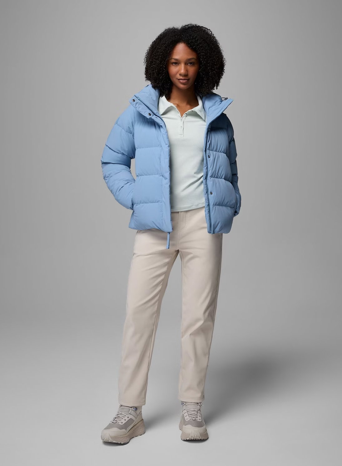 A woman wearing a blue puffer jacket and white pants.