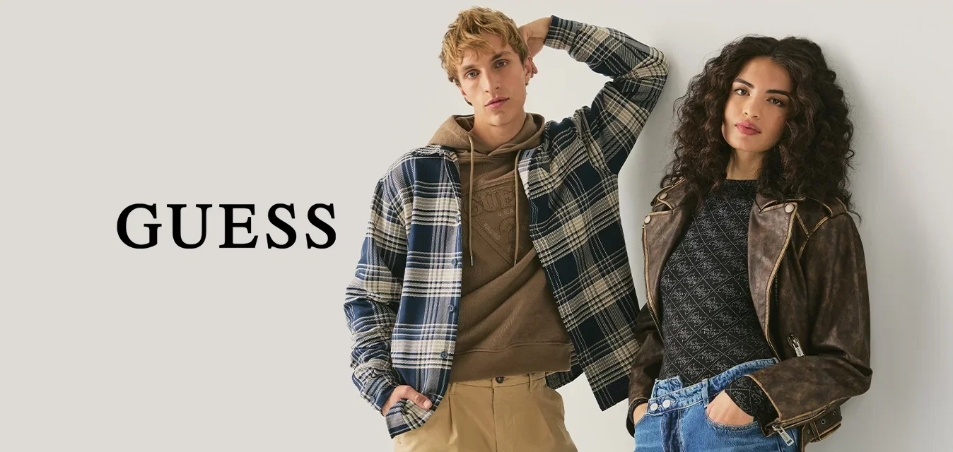 Twee jongvolwassenen leunen tegen een muur, gekleed in casual herfstkleding: een geruit jack, een hoodie, khaki broeken en een leren jas met spijkerbroek.