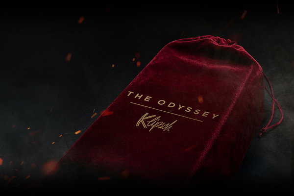 Red velvet bag with gold lettering for Klipsch x The Odyssey speaker on a fiery and smokey background.