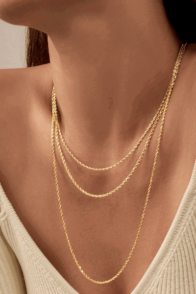 Close up of model wearing three layers of gold chain necklaces.