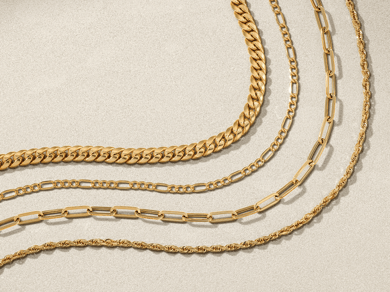 Layers of yellow gold chain necklaces on textured background.