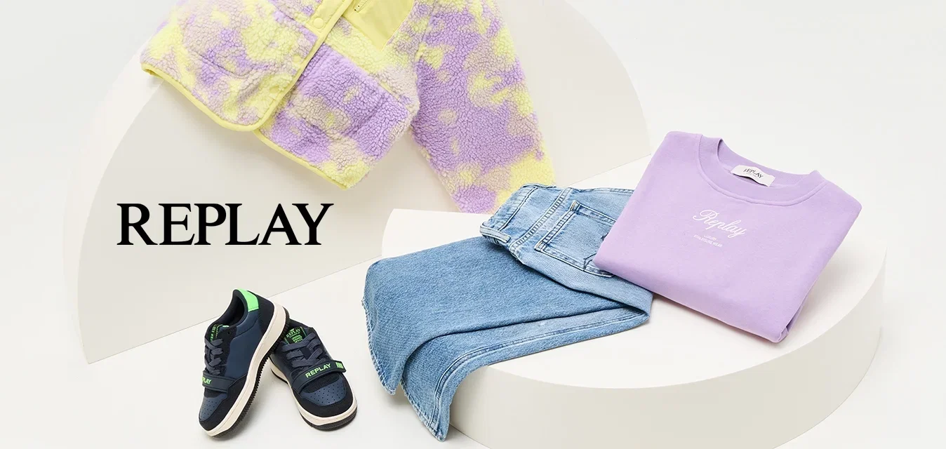 Paarse en gele donzige jas, lavendelkleurig sweatshirt, blauwe jeans en marineblauwe sneakers met groene accenten, opgesteld op een gebogen witte display.