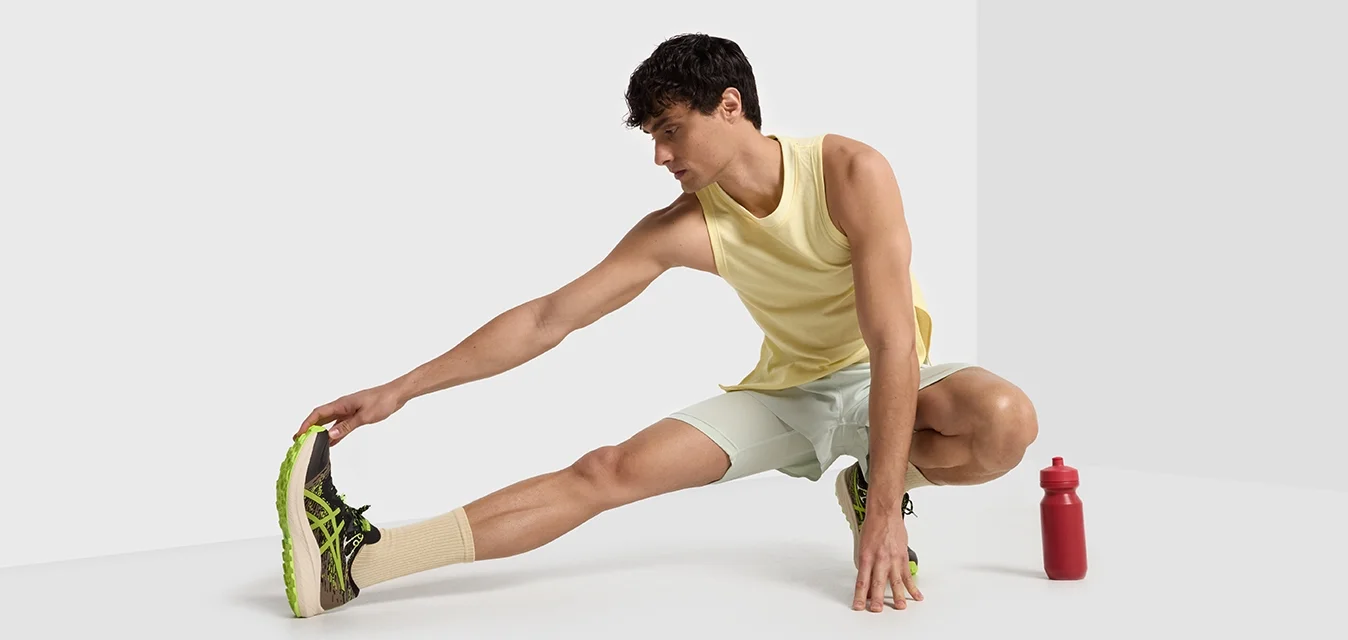 Sportoutfit bestaande uit een gele mouwloos T-shirt, lichtgroene shorts en zwart-groene hardloopschoenen, met een rode waterfles erbij.
