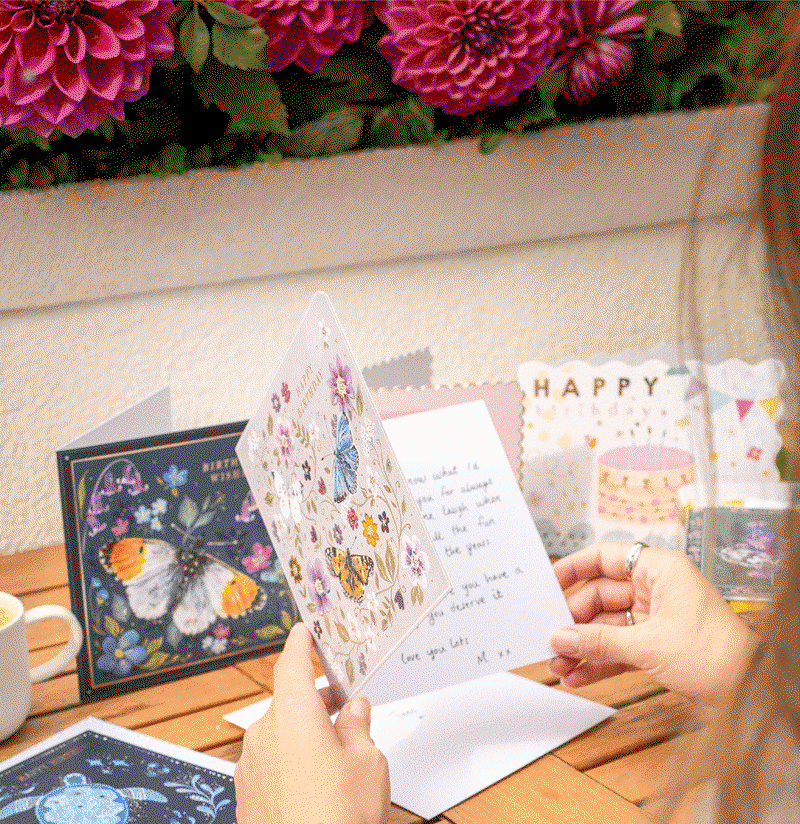 A handwritten birthday card being opened amongst Whistlefish birthday cards and flowers. Shop 11 everyday cards for £12.