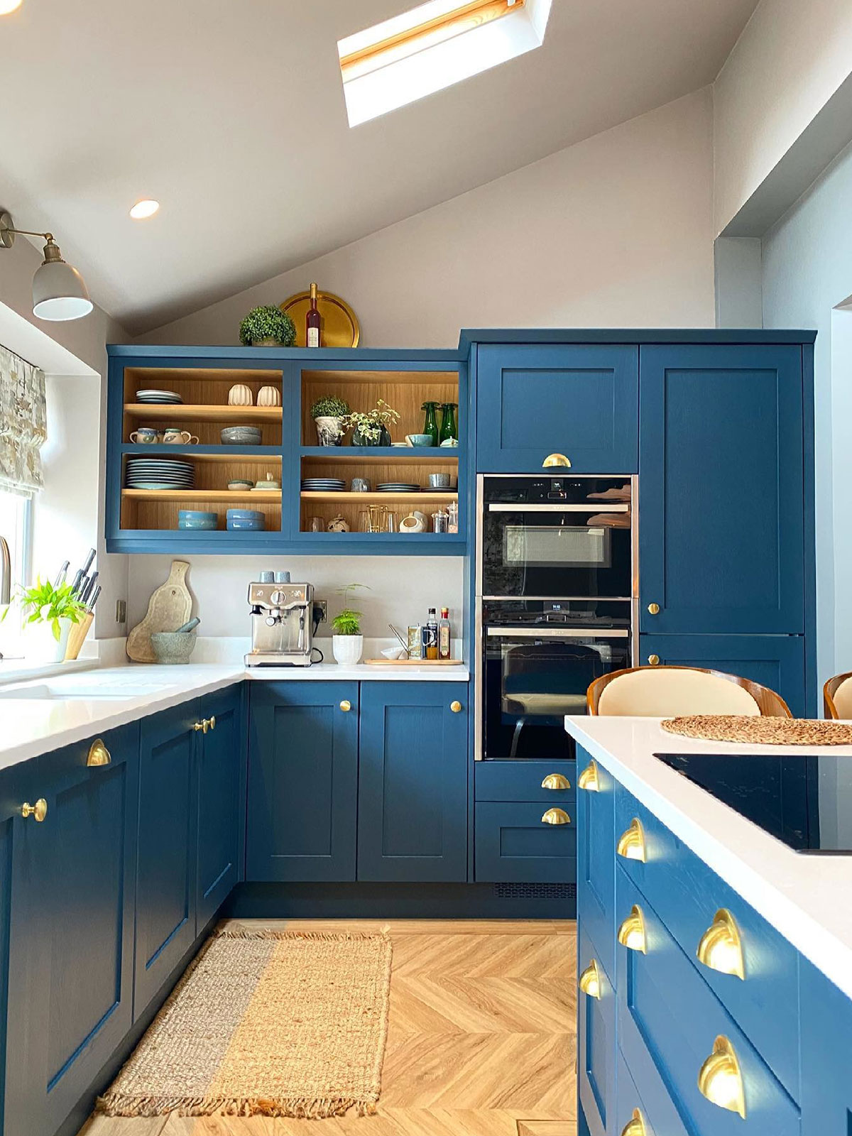 A traditional kitchen with light, cream walls and rich blue cabinets. The combination creates a calm feel, reminiscent of floating in a peaceful ocean. The floor is a wooden herringbone pattern, which adds both warmth and sophistication.
