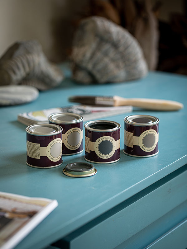 Four Farrow & Ball paint sample pots, including 'Down Pipe,' 'Mole's Breath,' 'Pavilion Gray,' and 'Purbeck Stone,' arranged on a turquoise chest of drawers.