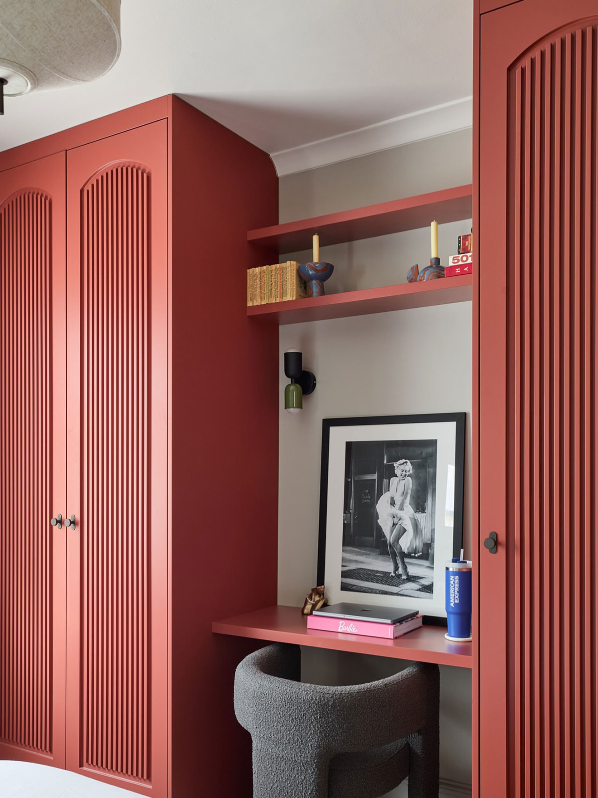 A striking, modern office space with built-in storage painted in a vibrant red. The shade is bursting with energy, give the room a lively feel. The desk is set into an alcove between the storage, and it’s also painted in the same shade. On the desk is a framed photograph of Marilyn Monroe.
