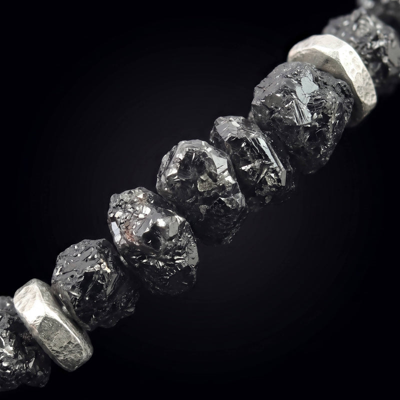 Close-up of raw black diamond with irregular surfaces and silver accents.